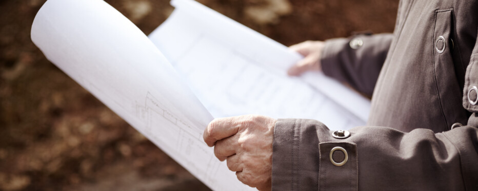 Papir med byggeplan holdes af person i jakke